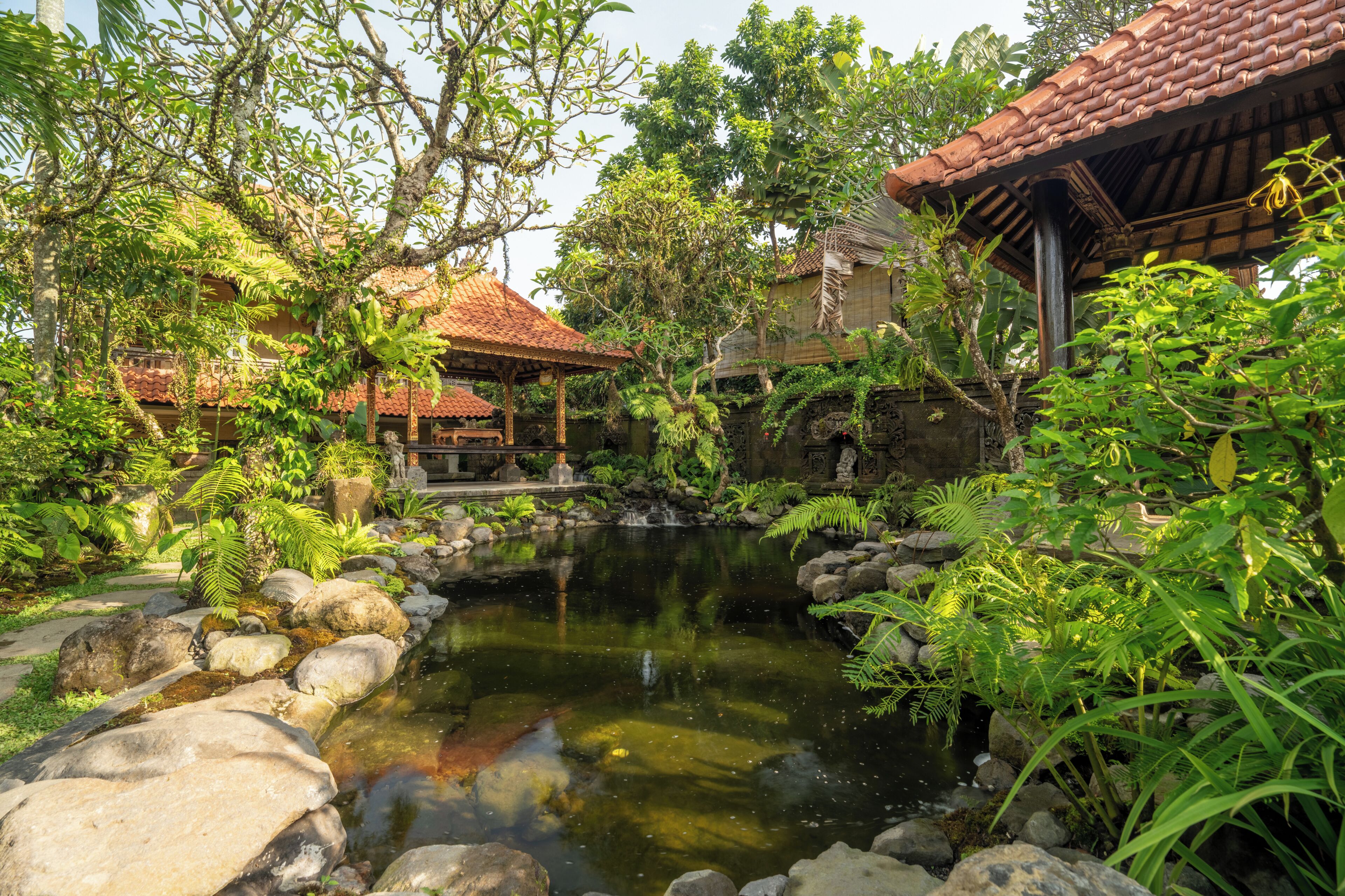 A serene garden with a pond, stone pathway, and traditional-style buildings.