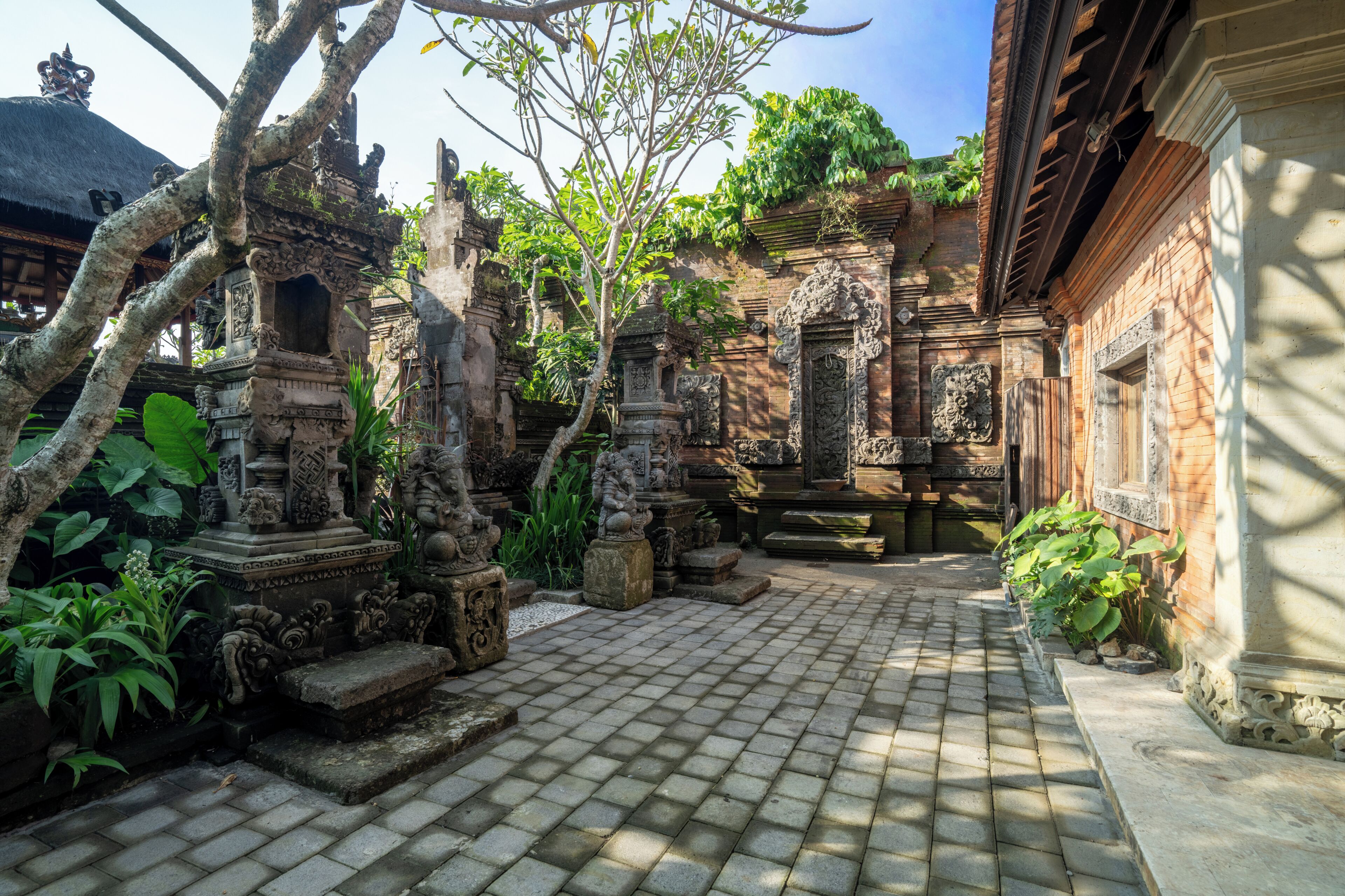 A courtyard with stone statues, a thatched-roof structure, and a brick building.
