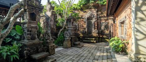 A courtyard with stone statues, a thatched-roof structure, and a brick building.