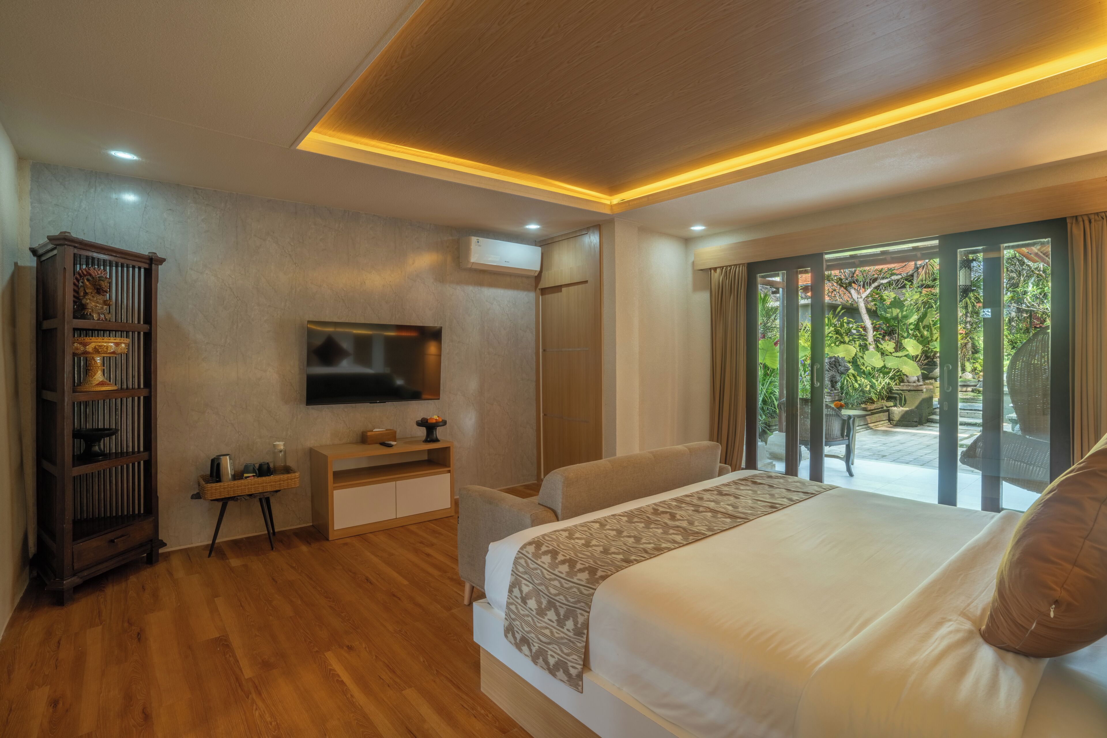 A bedroom with a bed, a TV, a wooden cabinet, and a sliding glass door leading to an outdoor area.