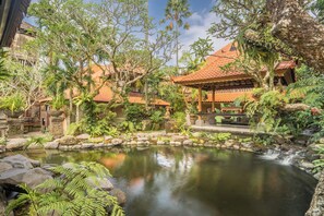 A traditional building with a tiled roof, surrounded by lush greenery and a small pond with a waterfall.