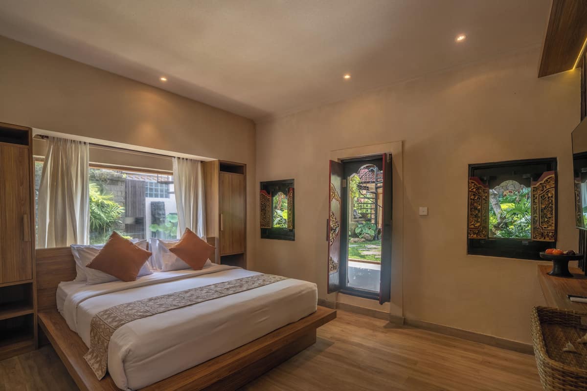 Quarto com cama grande, janela com cortinas, porta para o exterior e dois quadros pendurados na parede.