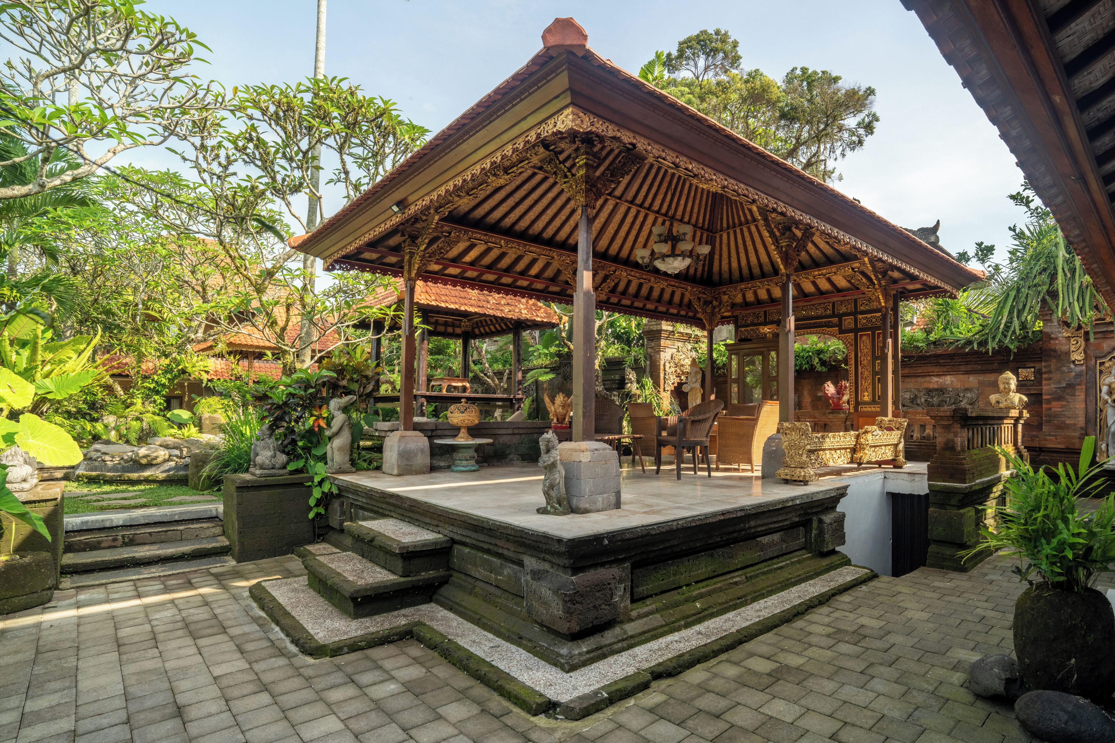 A traditional pavilion with a tiled floor, surrounded by stone steps and potted plants.