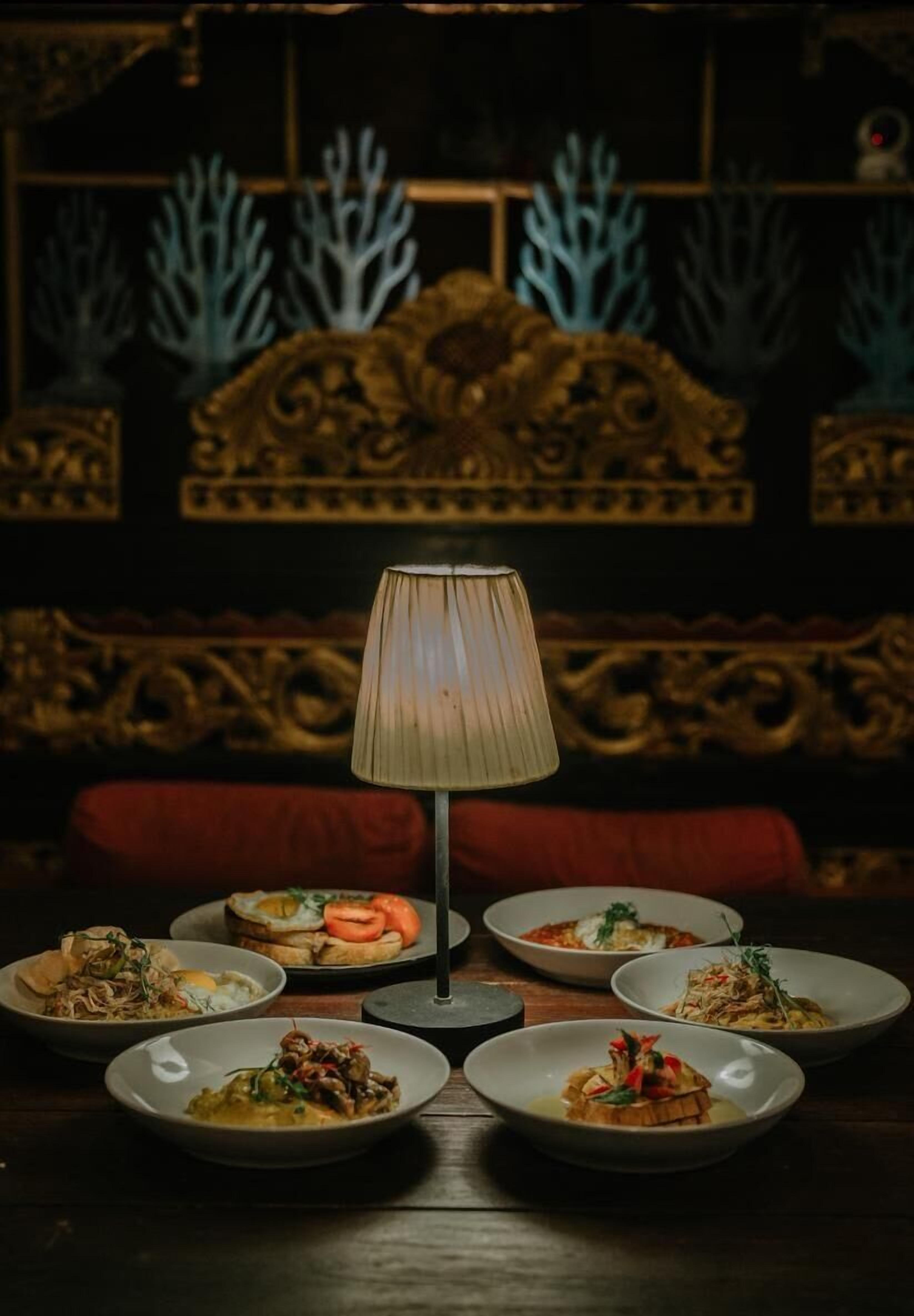 A dining table with multiple plates of food, a lamp, and a decorative headboard in the background.