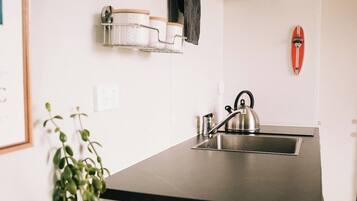 A compact kitchen with a black countertop, a kettle, a small sink, and a potted plant.