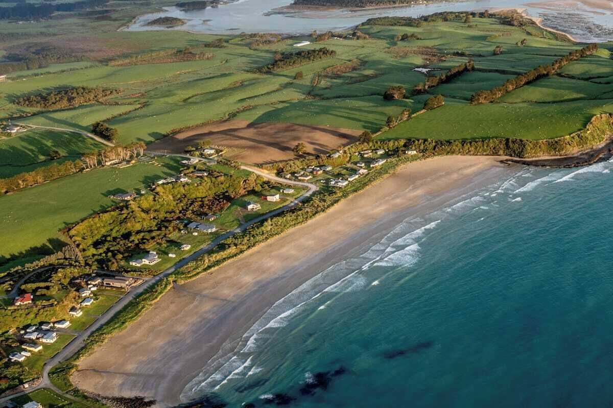 Luftaufnahme eines Küsten-Golfplatzes mit Sandstrand, grünen Spielbahnen und Wohngebieten.