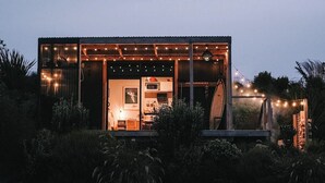 Una casa moderna con un amplio ventanal, una terraza de madera y luces colgantes.