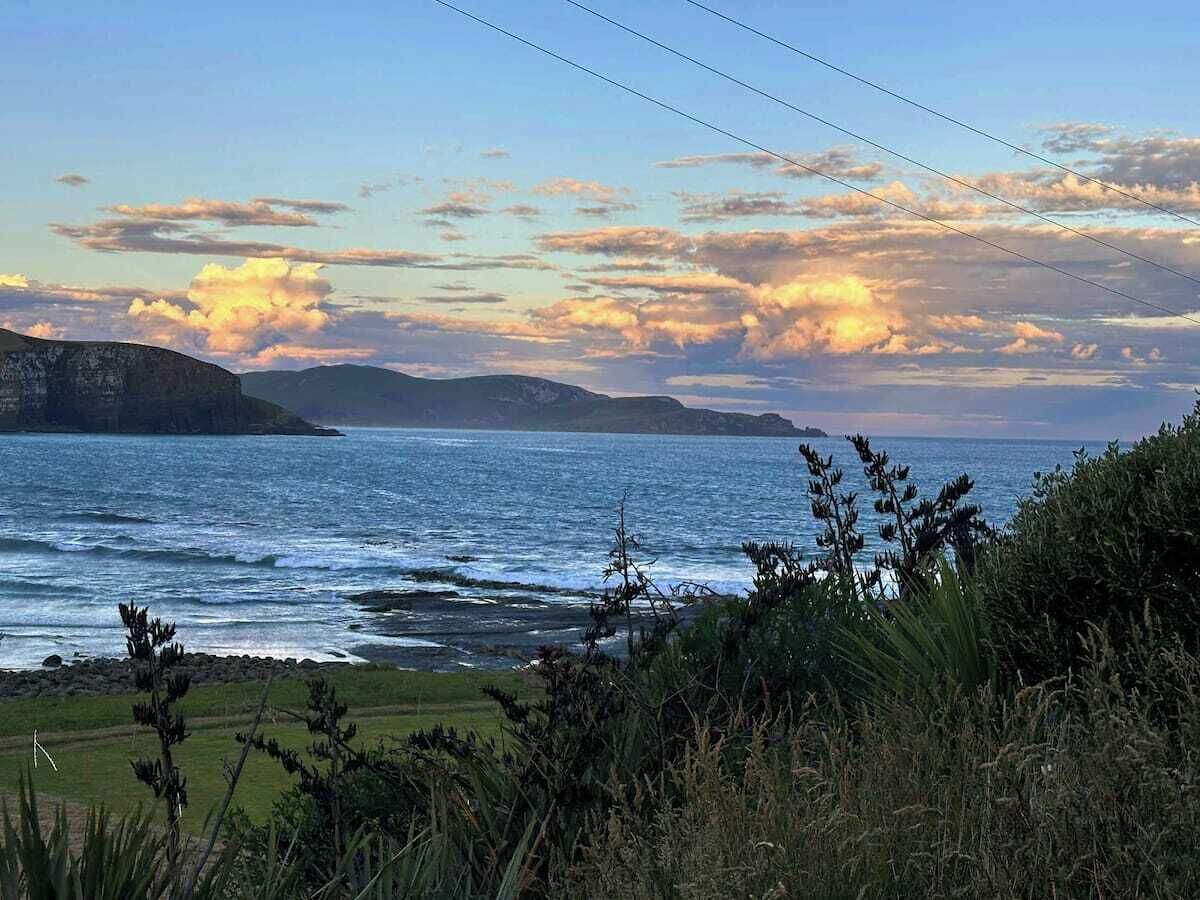 A coastal landscape with a view of the sea, distant hills, and a grassy foreground.