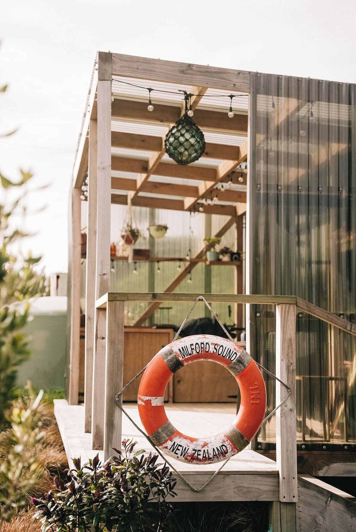 Eine Holzhütte mit einem Rettungsring, auf dem 'MELFORD SOUND NEW ZEALAND' steht, der an einem Seil hängt.