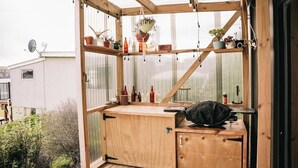 Una estructura de madera con cerramiento de vidrio, repisas con plantas y un banco.