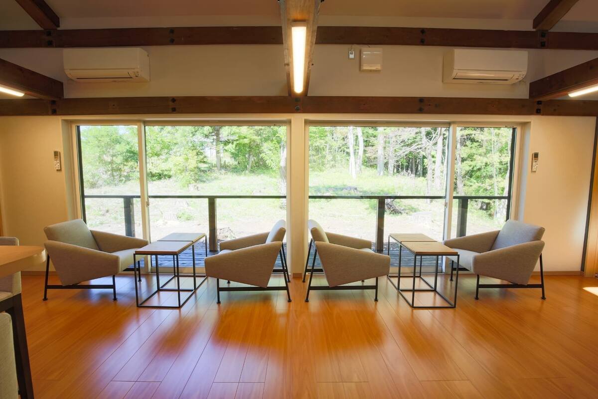 Une pièce dotée d’un plancher en bois, de deux canapés, d’une table et de grandes fenêtres donnant sur un paysage verdoyant.