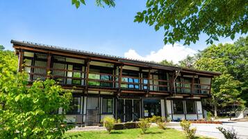 Un edificio tradicional japonés con estructura de madera, ventanas amplias y un jardín cuidado.