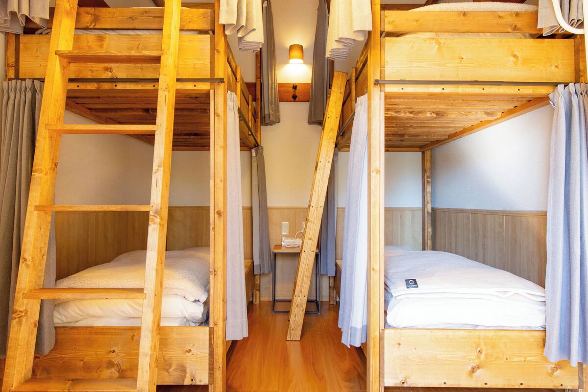 Une pièce avec deux lits superposés, un plancher en bois, une échelle, un luminaire suspendu et une petite table avec une chaise.
