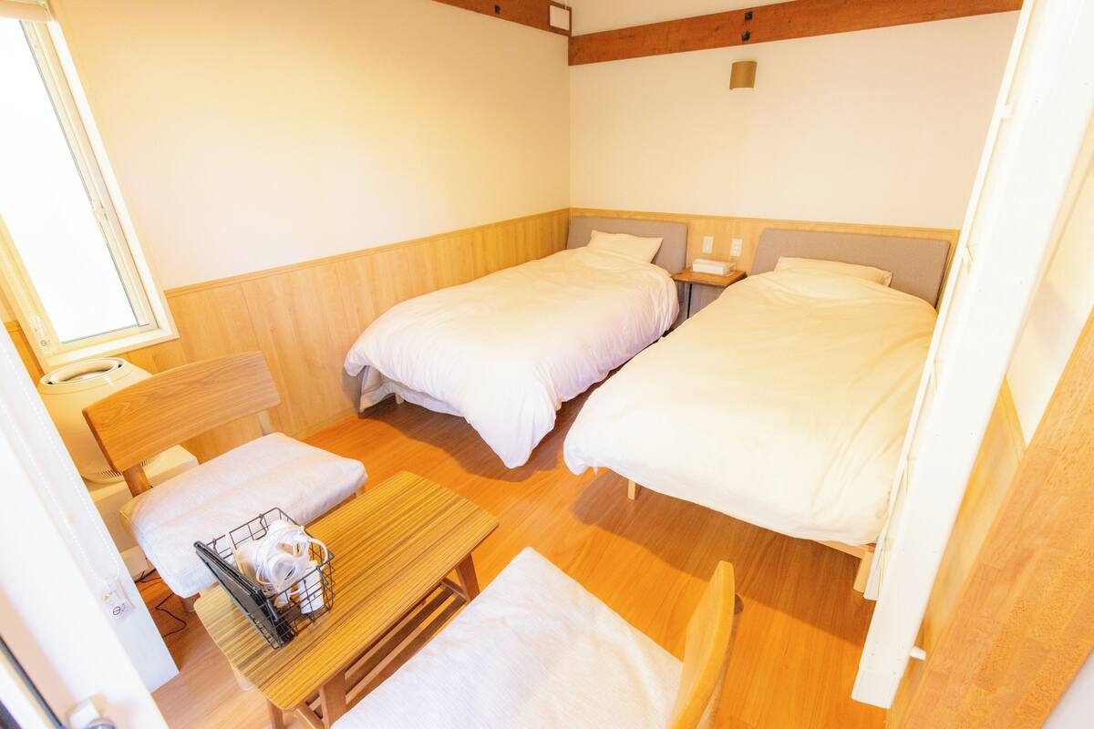 Une petite pièce propre, avec deux lits, une table et une chaise.