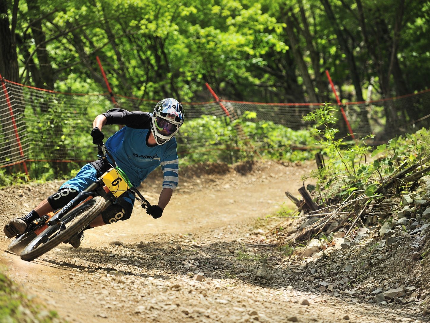 A mountain biker navigating a dirt trail with a fence on one side and trees in the background.