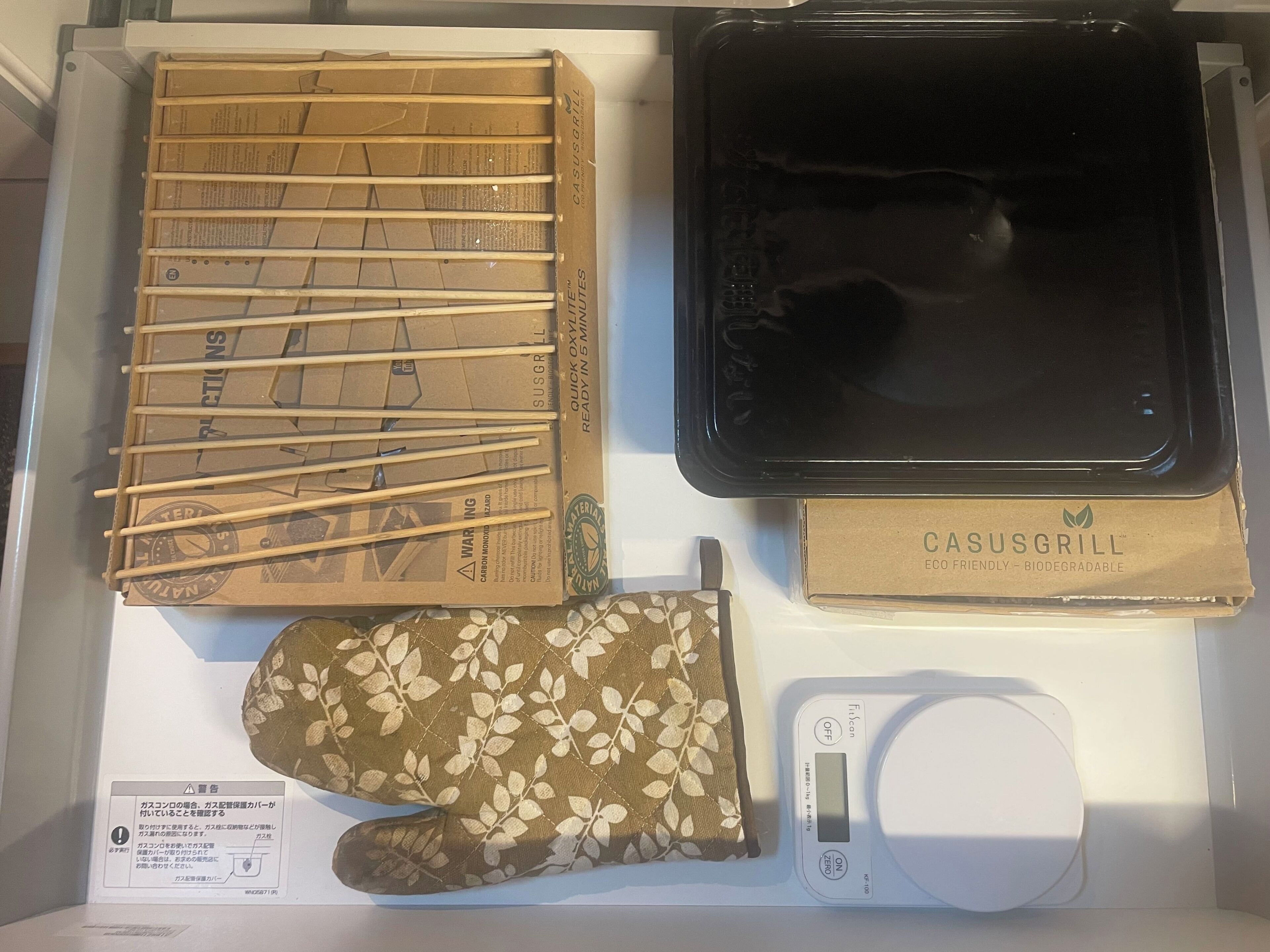 Una cocina con un microondas negro, un juego de palillos de madera, un horno con la marca Casus Grill y una balanza digital para cocina.