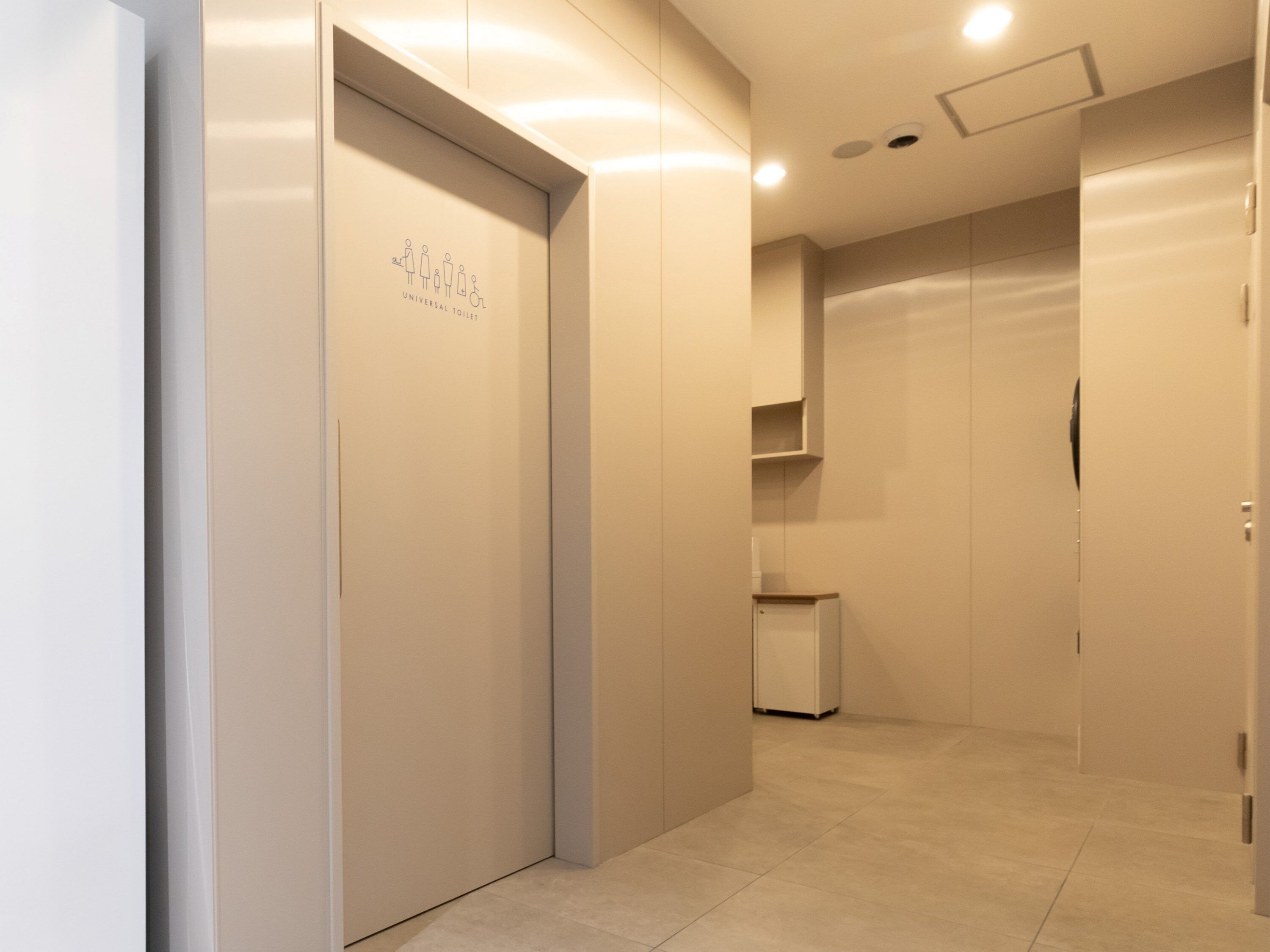 Un corridoio con un cartello che indica i servizi igienici accessibili, un cestino e una porta sulla destra.