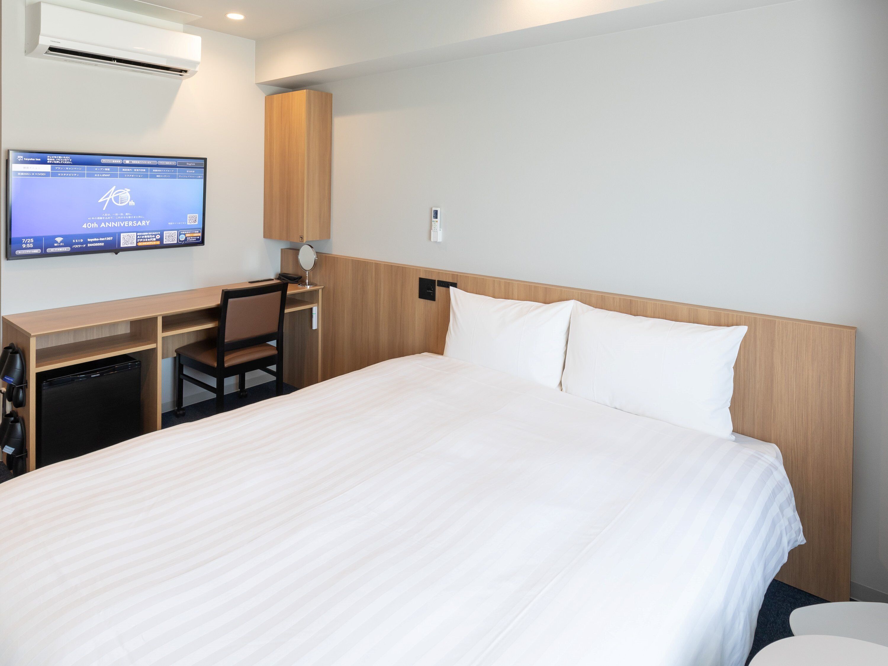 Una habitación de hotel con una cama, un escritorio, una silla, un televisor y un equipo de aire acondicionado.