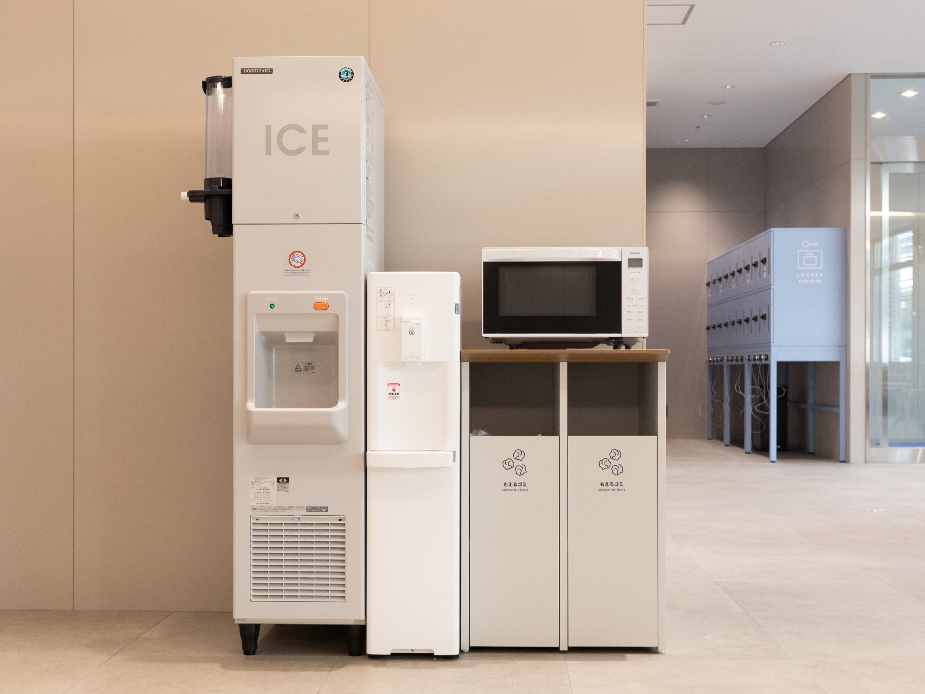 A water dispenser, a microwave, and a refrigerator with recycling symbols in a modern hotel setting.