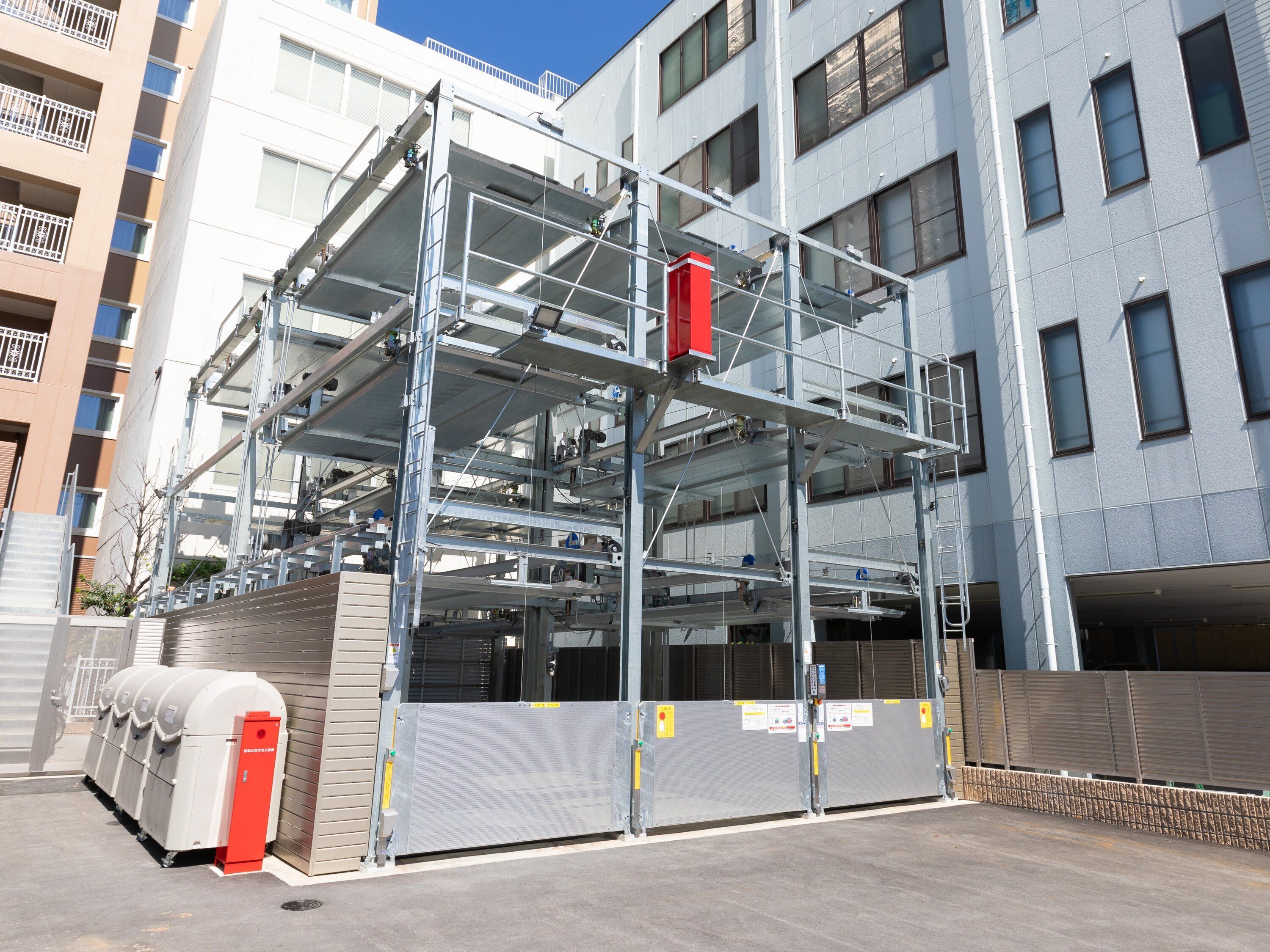 A multi-story building with a metal scaffolding structure, a gated entrance, and a parking area.
