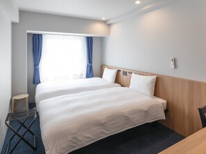 Een hotelkamer met twee bedden, een tafeltje, een stoel en een raam met gordijnen.