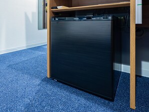 A compact, dark-colored refrigerator in a room with a blue carpet and wooden furniture.