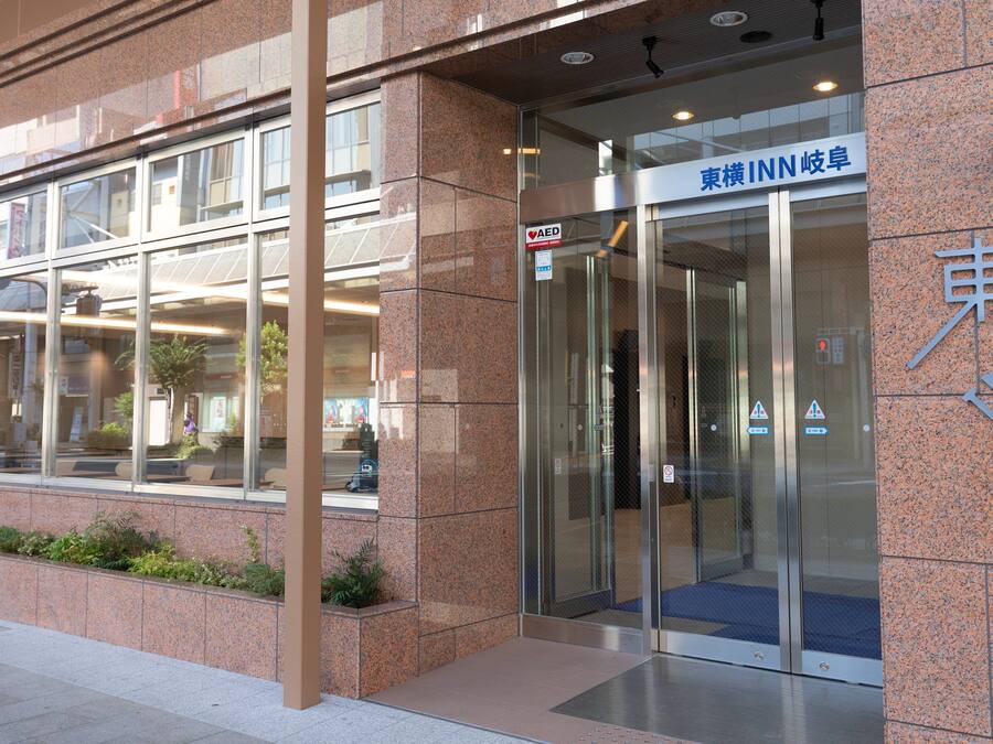A modern building entrance with a glass door, a sign indicating an AED, and a blue sign with Japanese characters.