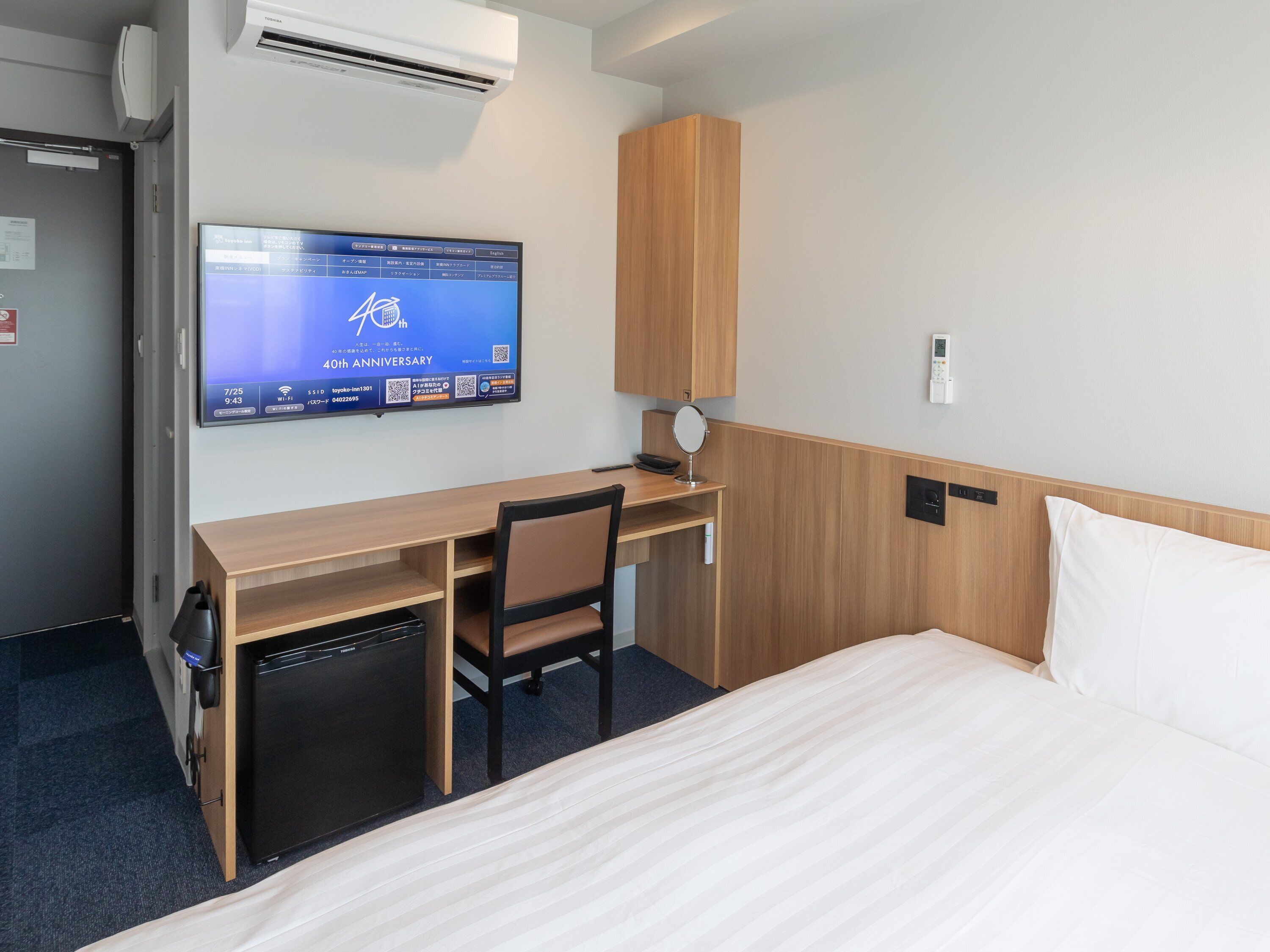Una habitación de hotel con cama, escritorio, silla, televisor y armario.