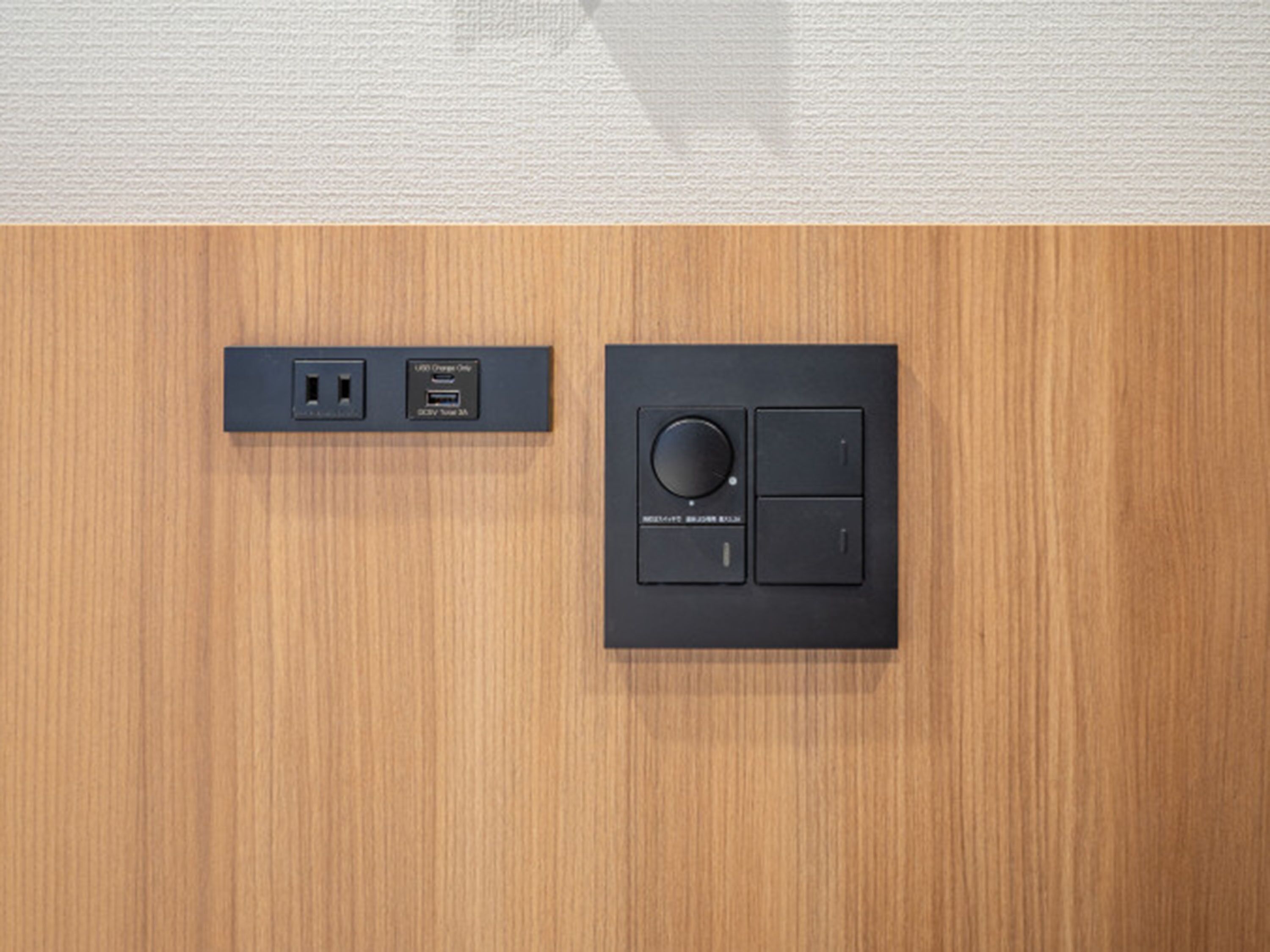 Een bedieningspaneel aan de muur met een ronde knop en twee knoppen, plus een USB-oplaadpoort met een label.