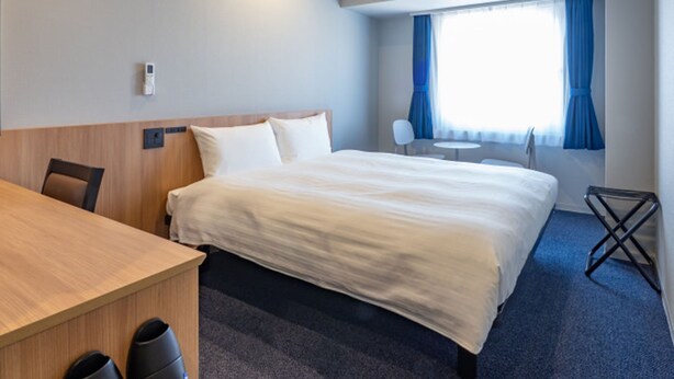 A hotel room with a bed, a desk, a chair, a small table, and a window with curtains.
