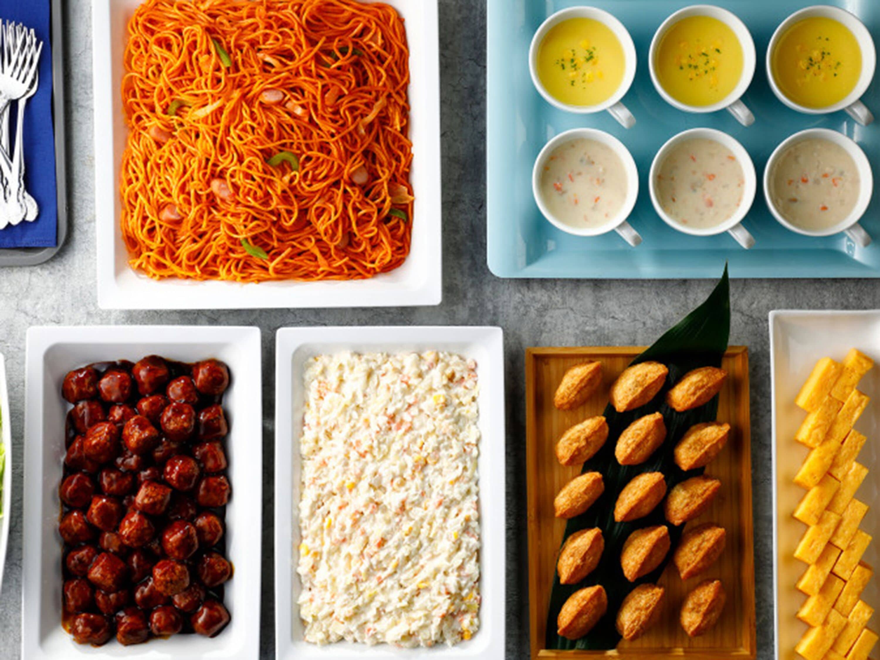 A variety of dishes including noodles, soup, meatballs, coleslaw, and pastries.