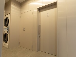 Een privélift met een deur waarop 'LADIES' staat en een wasmachine aan de muur in een gang.