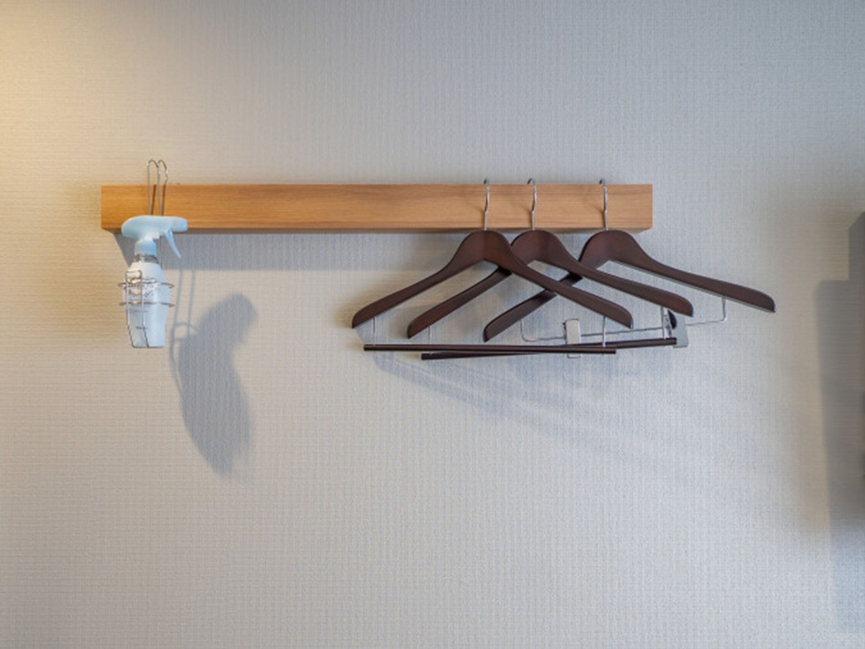 A wall-mounted wooden rack with three brown hangers and a spray bottle.