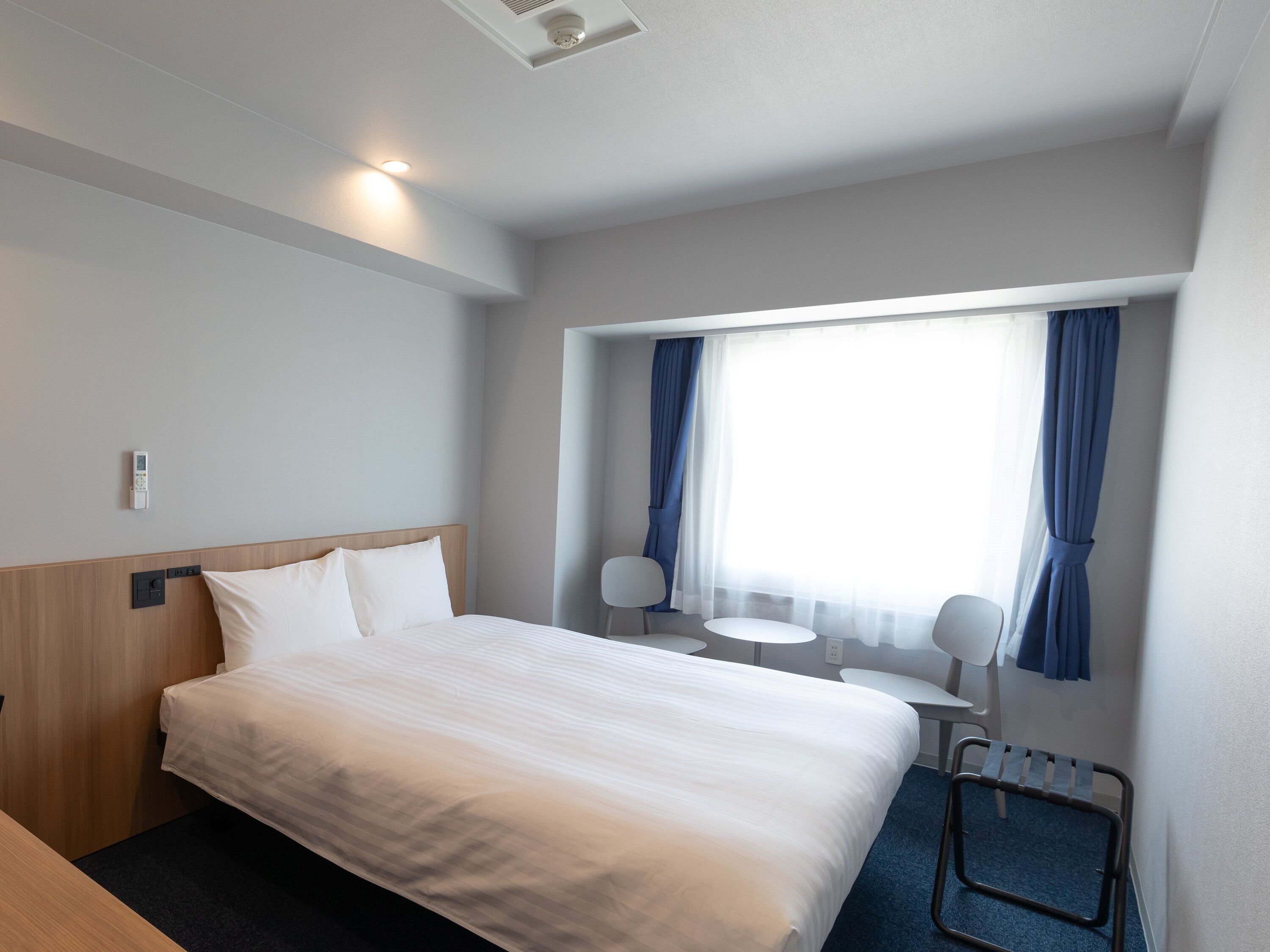 A hotel room with a bed, bedside table, lamp, and a window with curtains.