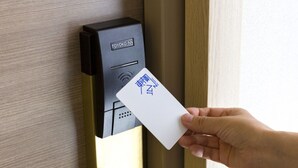 A hand holding a card in front of a digital keycard reader with 'TOYOKO INN' visible.