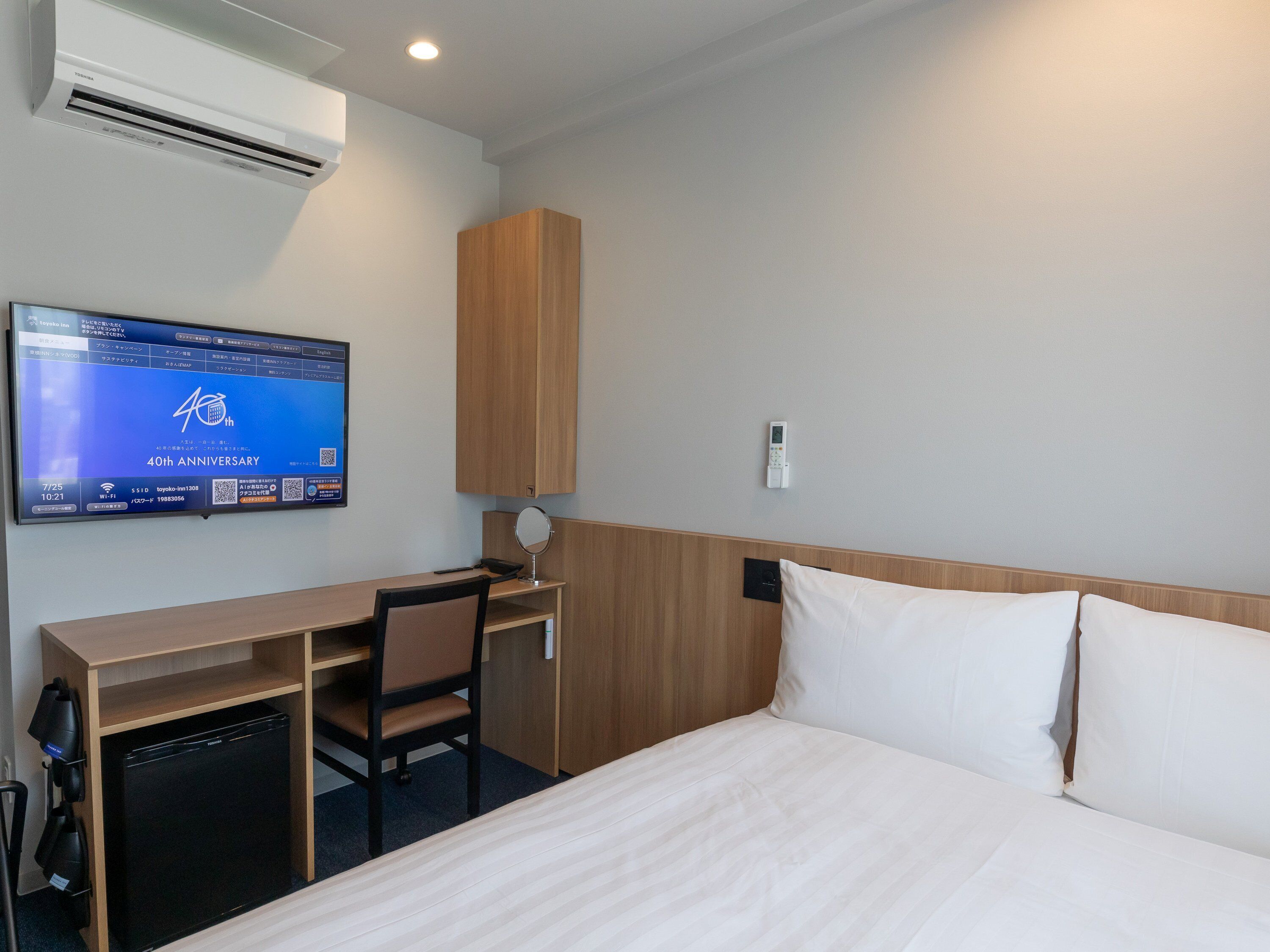 A hotel room with a bed, a desk, a chair, a television, and an air conditioning unit.