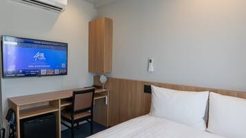 A hotel room with a bed, a desk, a chair, a television, and an air conditioning unit.