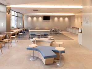 Eine moderne Cafeteria mit runden Tischen und Bänken, einer Wanduhr und einem an der Wand befestigten Flachbildfernseher.
