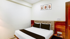 A bedroom with a bed, a nightstand, a wooden wardrobe, and three wall-mounted pictures. - Hotel O Kakatiya Hills Shree Adithya Luxury (Hyderabad)