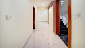 A hallway with a marble floor, wooden doors, and a staircase with a metal railing. - Hotel O Kakatiya Hills Shree Adithya Luxury (Hyderabad)