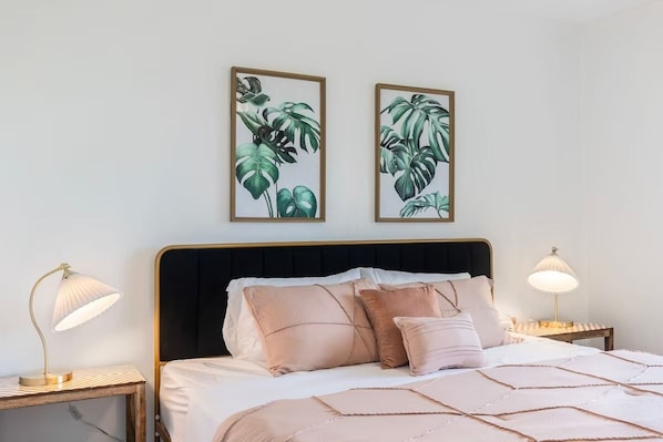 A bedroom with a bed, two bedside lamps, and two framed botanical prints on the wall.