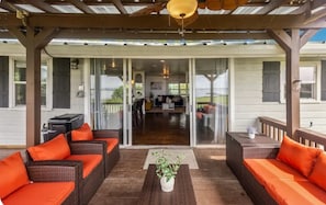 An outdoor patio with wicker furniture and orange cushions, a ceiling fan, and a view into the house.