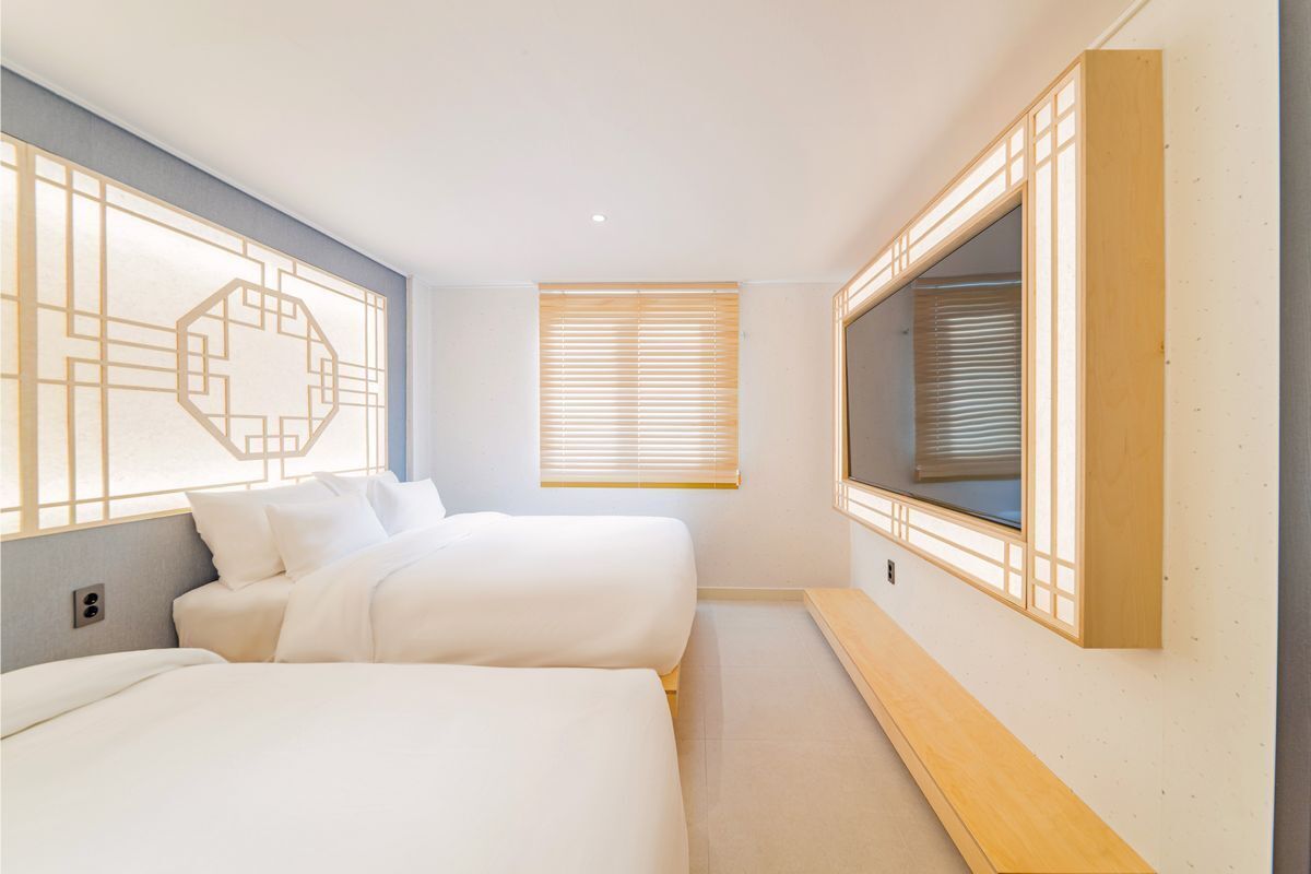 A hotel room with two beds, a TV, and a window with blinds.
