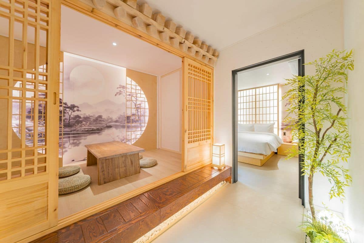 Una habitación tradicional japonesa con suelo de tatami, una mesa de madera baja, una cama con ropa blanca y vistas a un paisaje montañoso a través de un shoji.