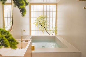 Un baño moderno con una bañera grande, una puerta de madera y una ventana con vistas a un árbol.