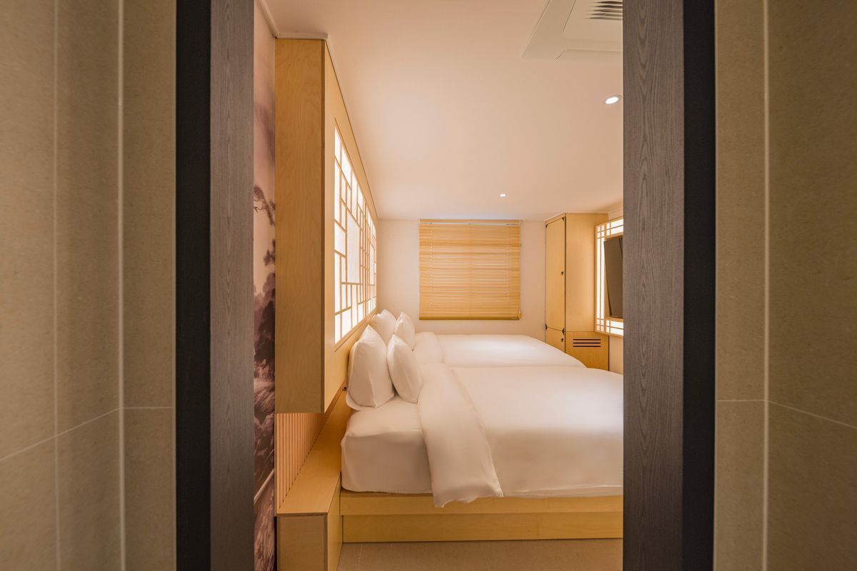 Habitación de hotel con una cama grande, cabecera de madera, ventana con persianas y televisor montado en la pared.