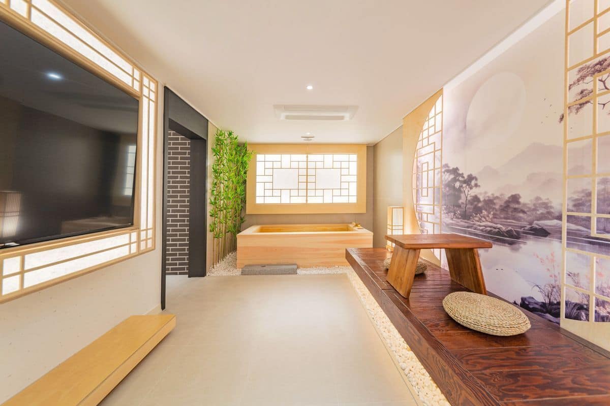 Un baño moderno con bañera, un banco de madera y un amplio ventanal con vistas a un paisaje montañoso.