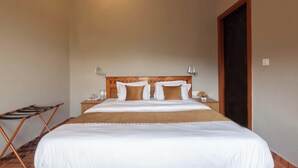 A neatly made bed with white linens and a brown throw, a wooden headboard, bedside lamps, and a wooden folding chair. - Alaya Stays Amara Aether (Naina Range)