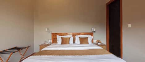 A neatly made bed with white linens and a brown throw, a wooden headboard, bedside lamps, and a wooden folding chair.