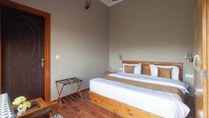 A bedroom with a wooden bed, a nightstand, a small table with a vase, a ceiling fan, and a wooden door. - Alaya Stays Amara Aether (Naina Range)